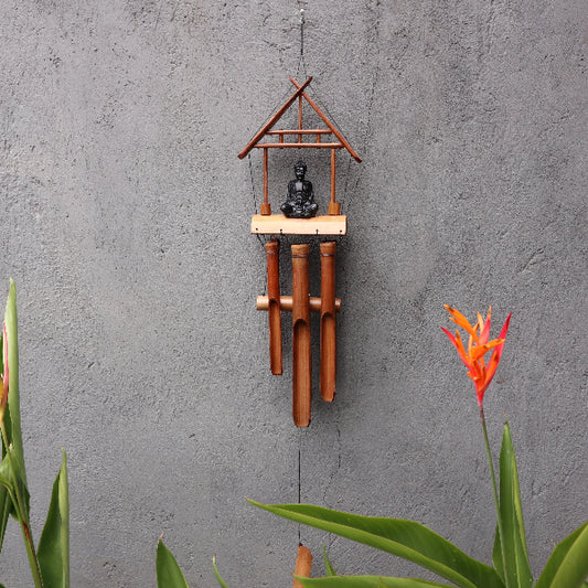 Bamboo wind chime with Buddha statue against a gray wall