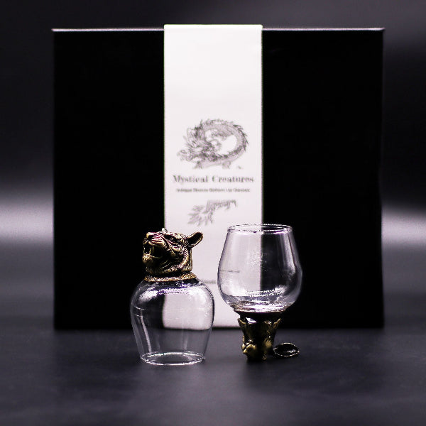 Two glass containers with gold animal-shaped bases in front of a black box labeled 'Mystical Creatures'.