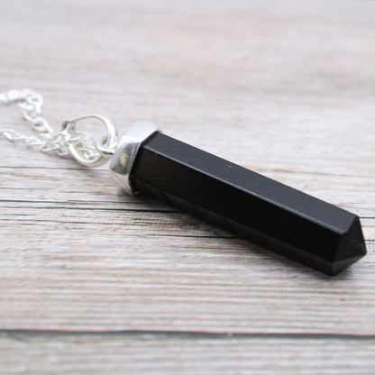Black crystal pendant on a silver chain against a wooden background