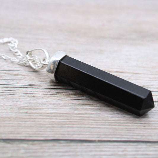 Black crystal pendant on a silver chain against a wooden background