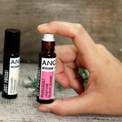 Hand holding a small rollerball bottle labeled 'ANC Wisdom' with another bottle in the background.