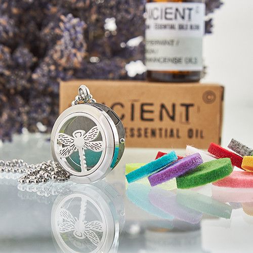 Silver dragonfly pendant necklace with a box of essential oils and colorful soap bars in the background.