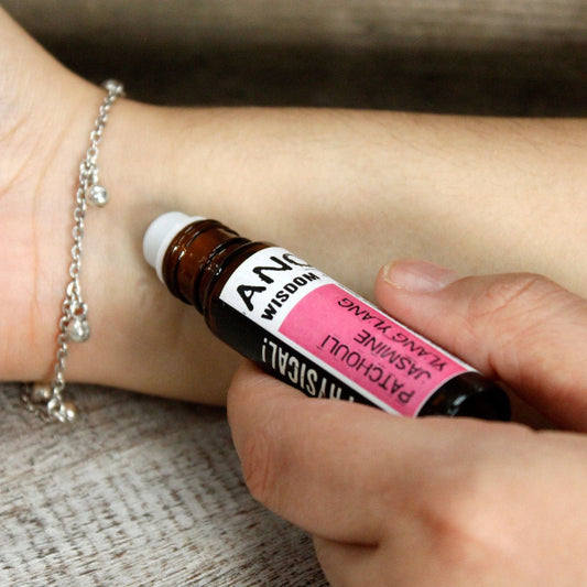 Hand holding a small bottle of essential oil near a wrist with a bracelet.