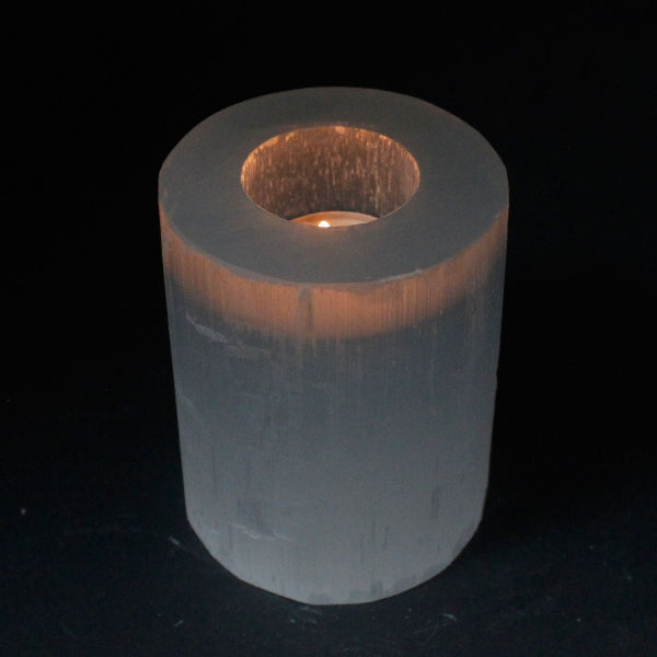 Cylindrical selenite candle holder with a candle inside on a black background