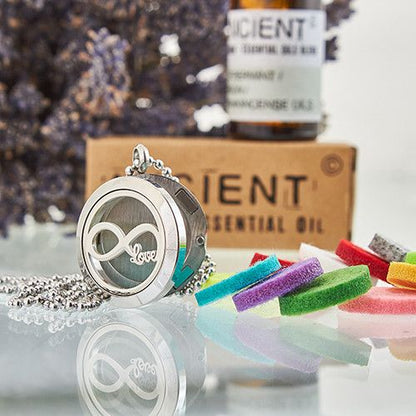 Necklace with a locket and colorful charms in front of a bottle of essential oil and a box labeled 'Gent'.