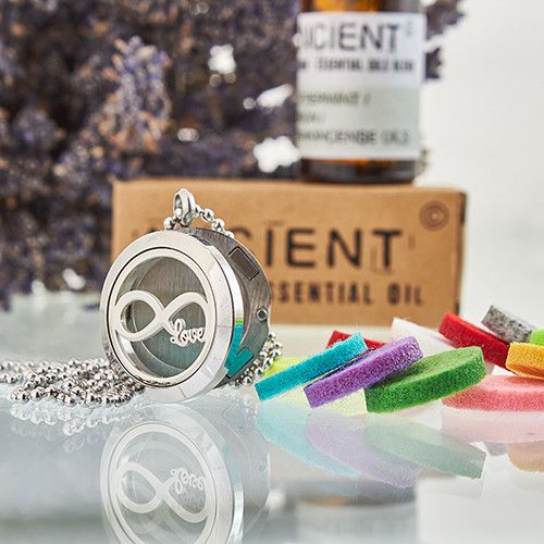 Necklace with a locket and colorful charms in front of a bottle of essential oil and a box labeled 'Gent'.