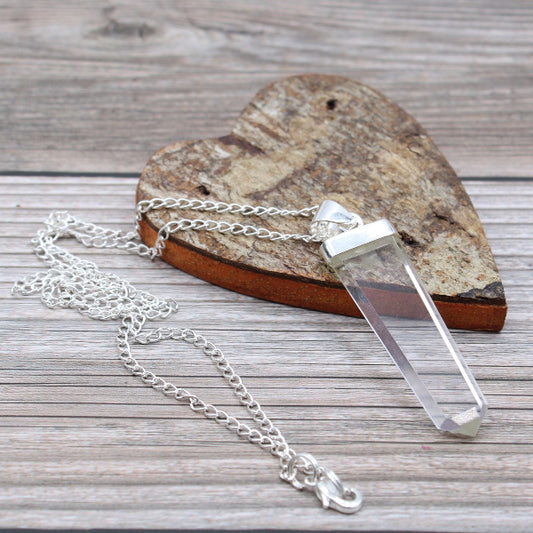Clear crystal pendant on a silver chain with a heart-shaped stone in the background