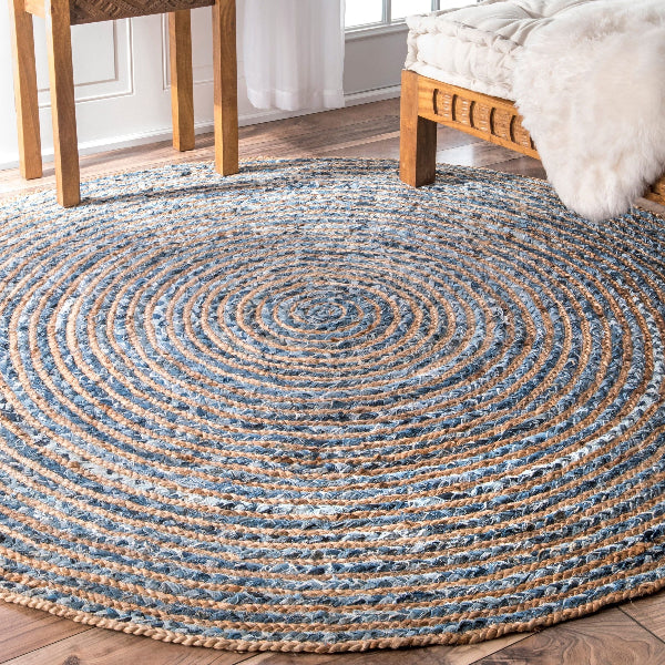 Round braided rug on a wooden floor with a wooden chair and bed in the background.