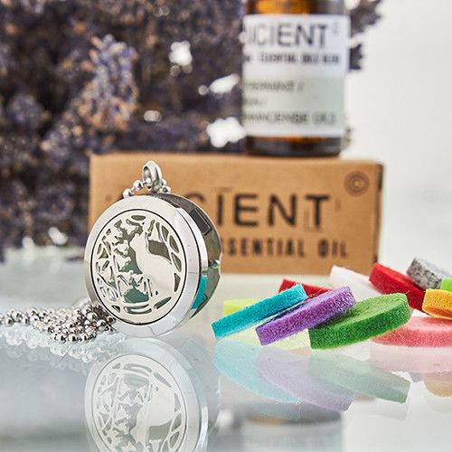 Silver locket with deer design on a reflective surface, with colorful bracelets and a bottle of essential oil in the background.
