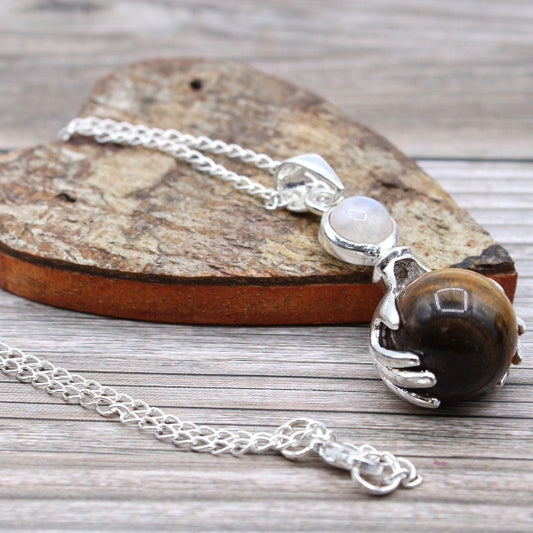 Necklace with a hand-shaped pendant holding a brown stone on a wooden surface