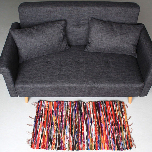 Gray sofa with two cushions on a light gray floor, colorful rug in front