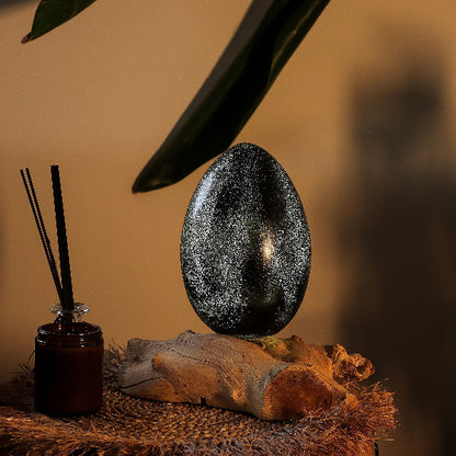 Decorative egg on a wooden base with a diffuser and leaves in the background