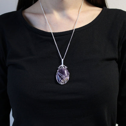 Person wearing a black shirt with a silver necklace featuring a purple pendant.