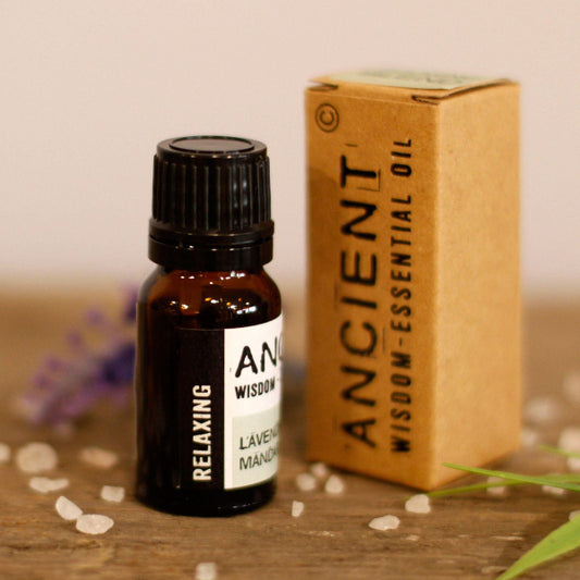 Bottle and box of Ancient Wisdom essential oil on a wooden surface with flowers in the background