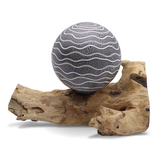 Decorative sphere with wavy pattern on a piece of driftwood against a white background