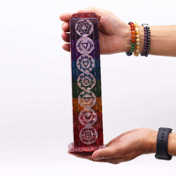 Hand holding a colorful Incense holder with chakra symbols against a white background