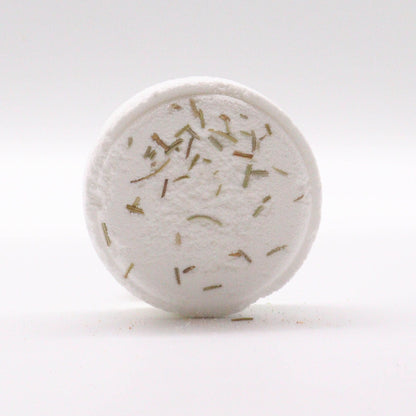 Round white bath bomb with green herbs on a light gray background