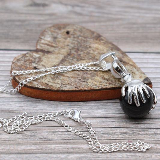 Necklace with a black pendant and silver chain on a wooden surface