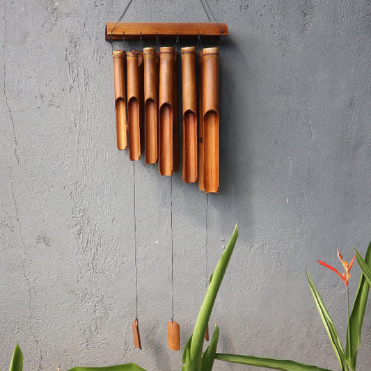 Bamboo wind chime hanging on a gray wall with plants in the foreground