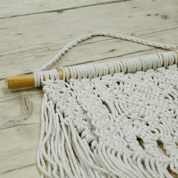 Macrame wall hanging with wooden dowel on a wooden surface