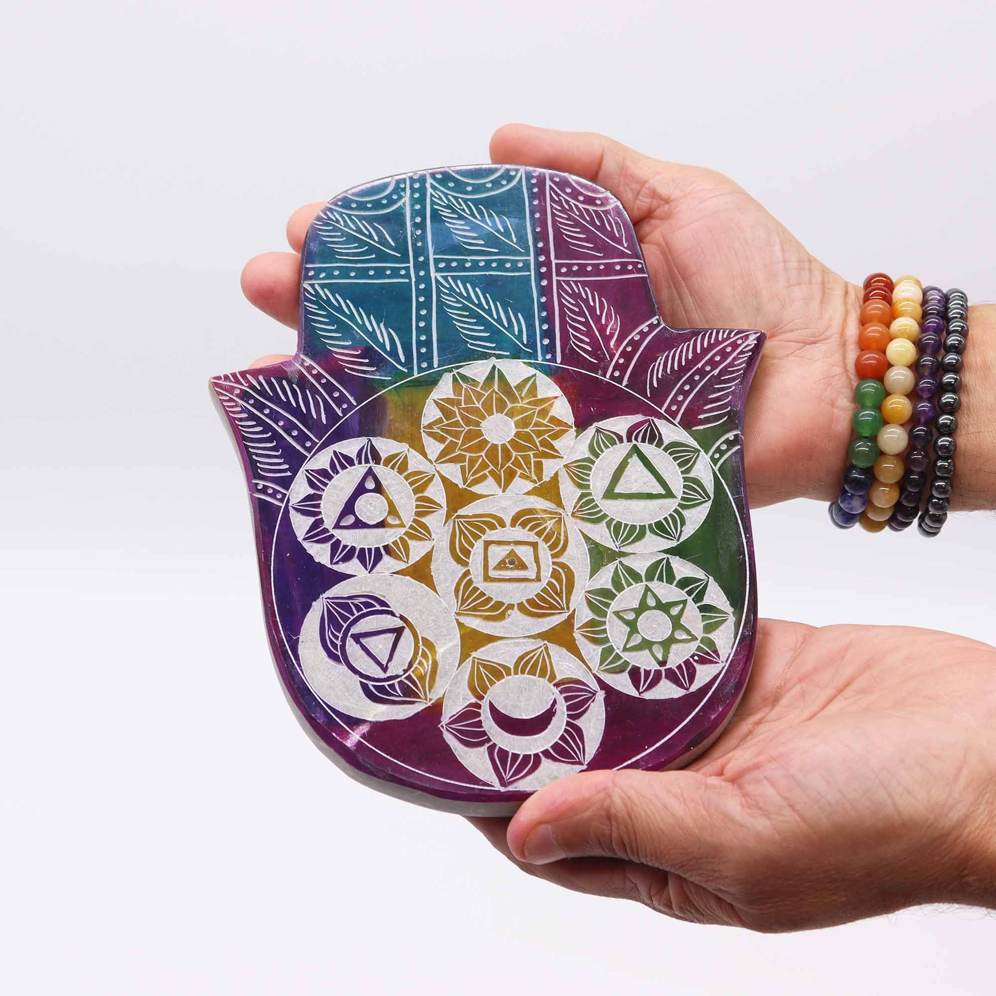 Hand holding a colorful Hamsa-shaped object with geometric patterns on a white background