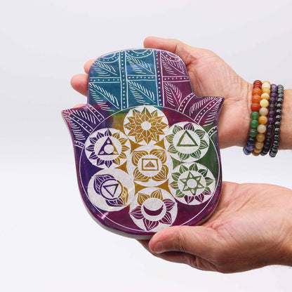 Hand holding a colorful Hamsa-shaped object with geometric patterns on a white background