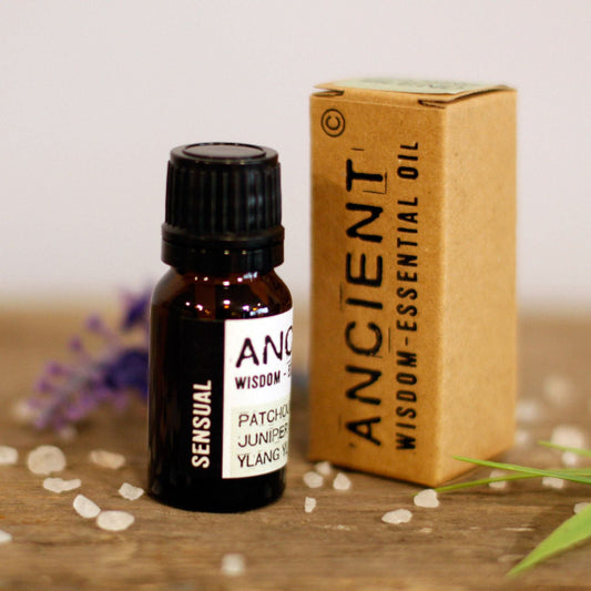 Essential oil bottle and box labeled 'Ancient Wisdom' on a wooden surface with flowers in the background.