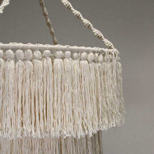 Close-up of a macrame plant hanger with white fringes on a gray background