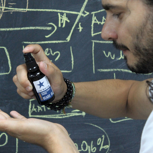 Person holding a bottle of beard oil in front of a chalkboard with drawings.